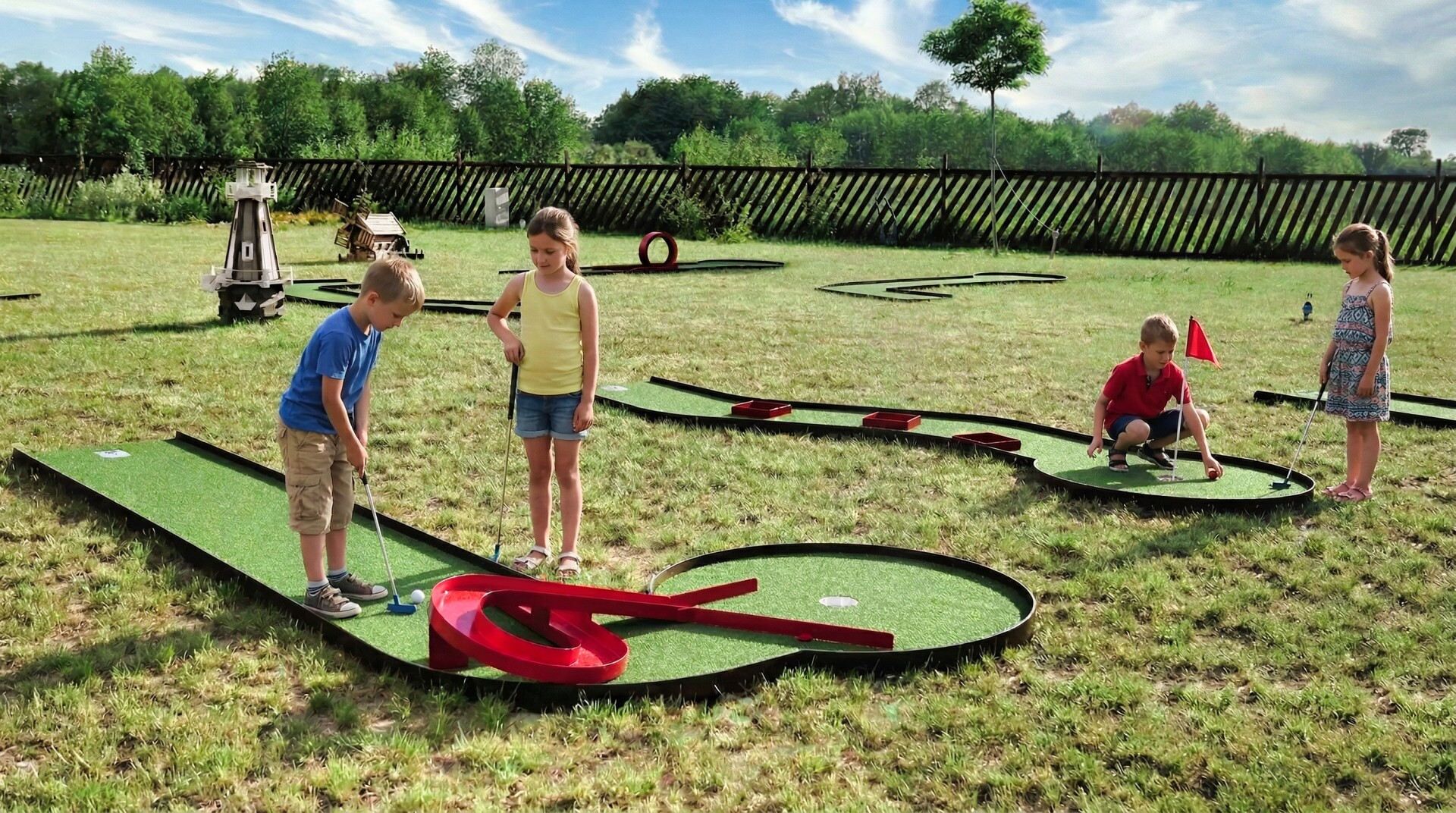 Um campo de mini golfe com grama sintética verde, obstáculos vermelhos e uma cerca de madeira ao fundo.