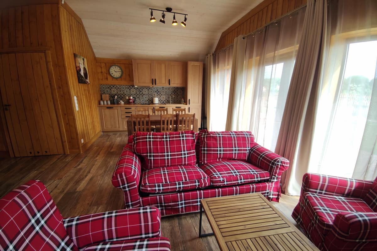 A cozy living area with a red plaid sofa set, a wooden coffee table, and a kitchen in the background.