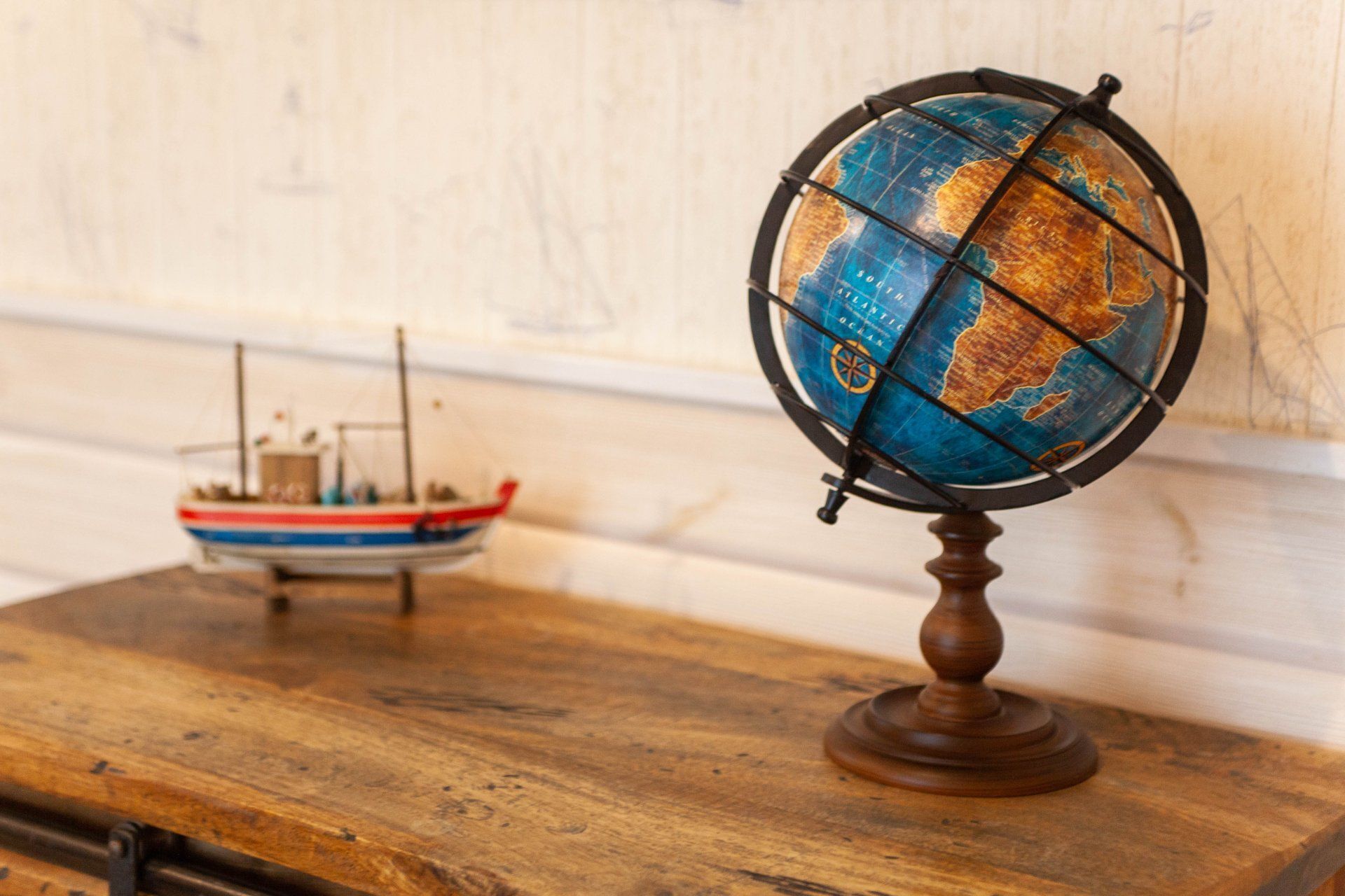 Un globe terrestre posé sur un socle en bois, avec une maquette de navire en arrière-plan.