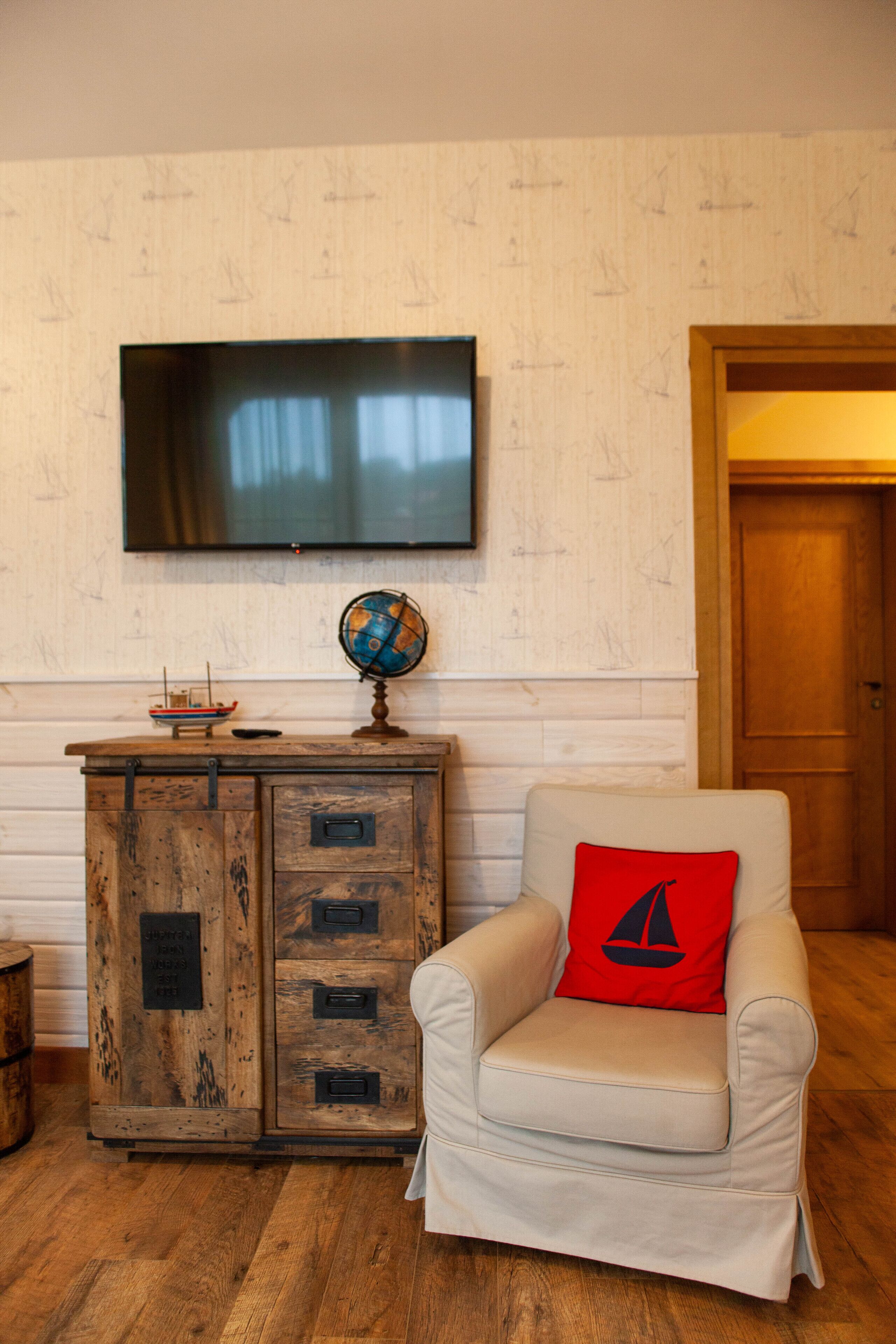 A room with a wooden cabinet, a television mounted on the wall, and a chair with a red pillow.