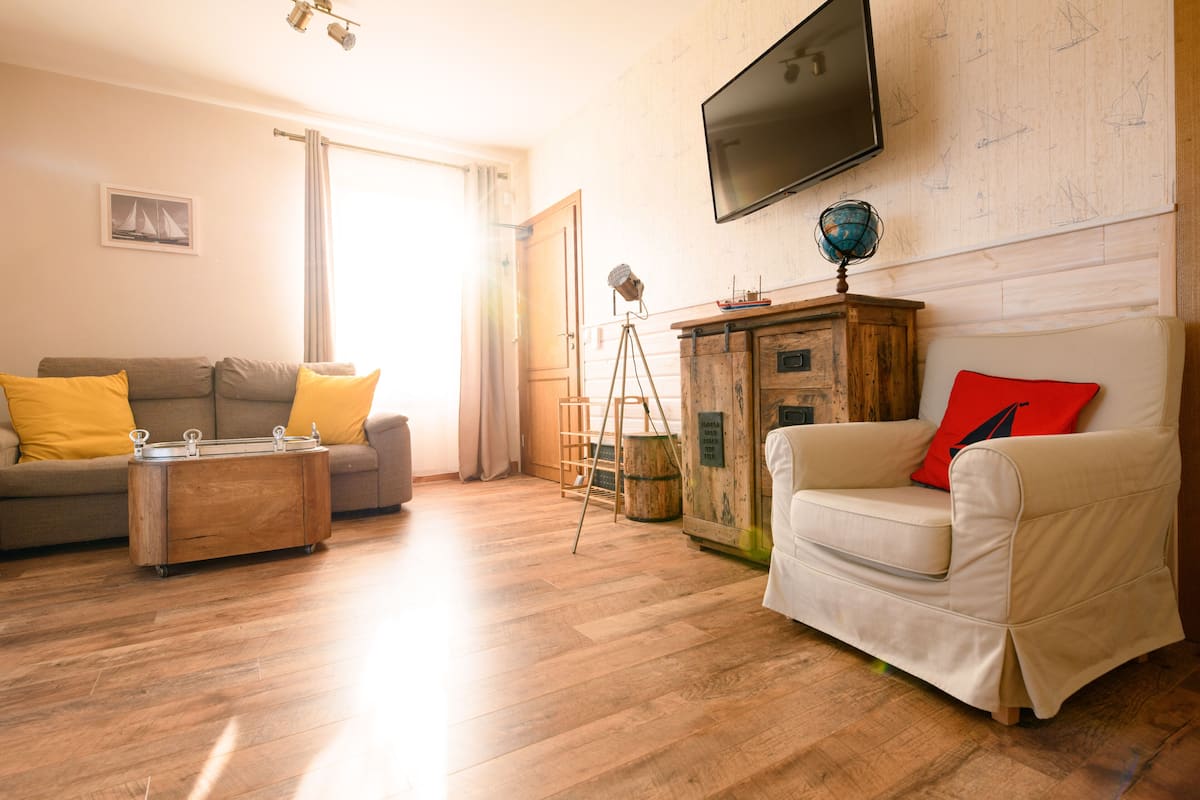 A living room with a wooden floor, a sofa, a chair, a coffee table, a television, and a globe on a cabinet.