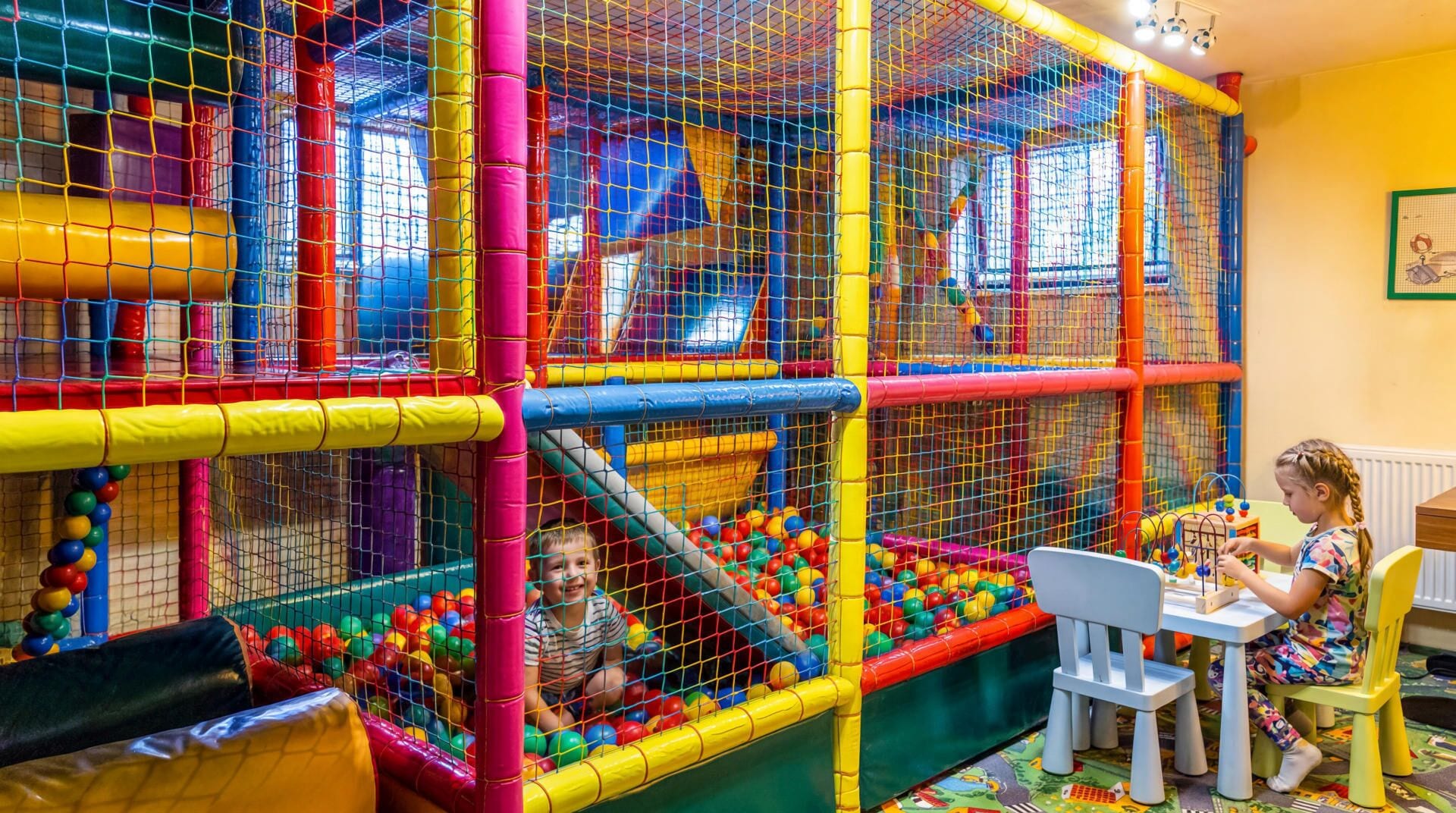 A play area with a netted enclosure, a ball pit, and a child playing at a table.