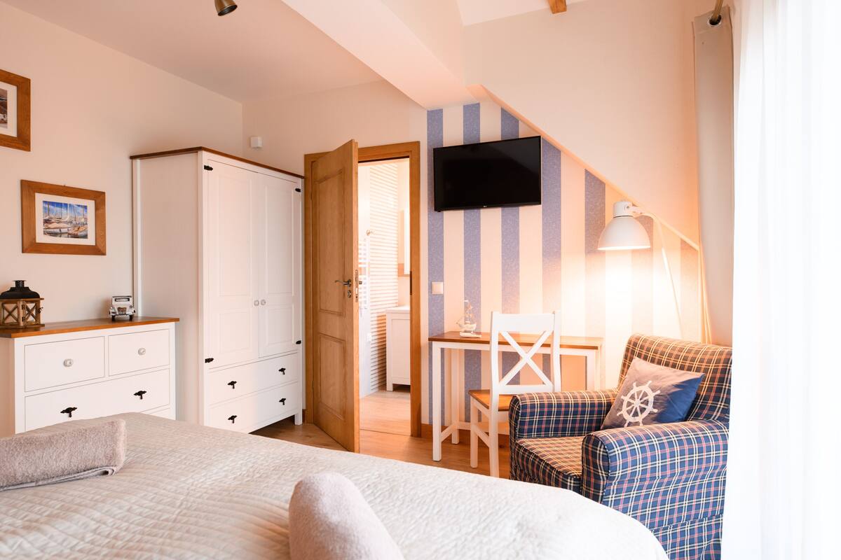 A bedroom with a bed, a desk, a chair, and a TV on the wall.