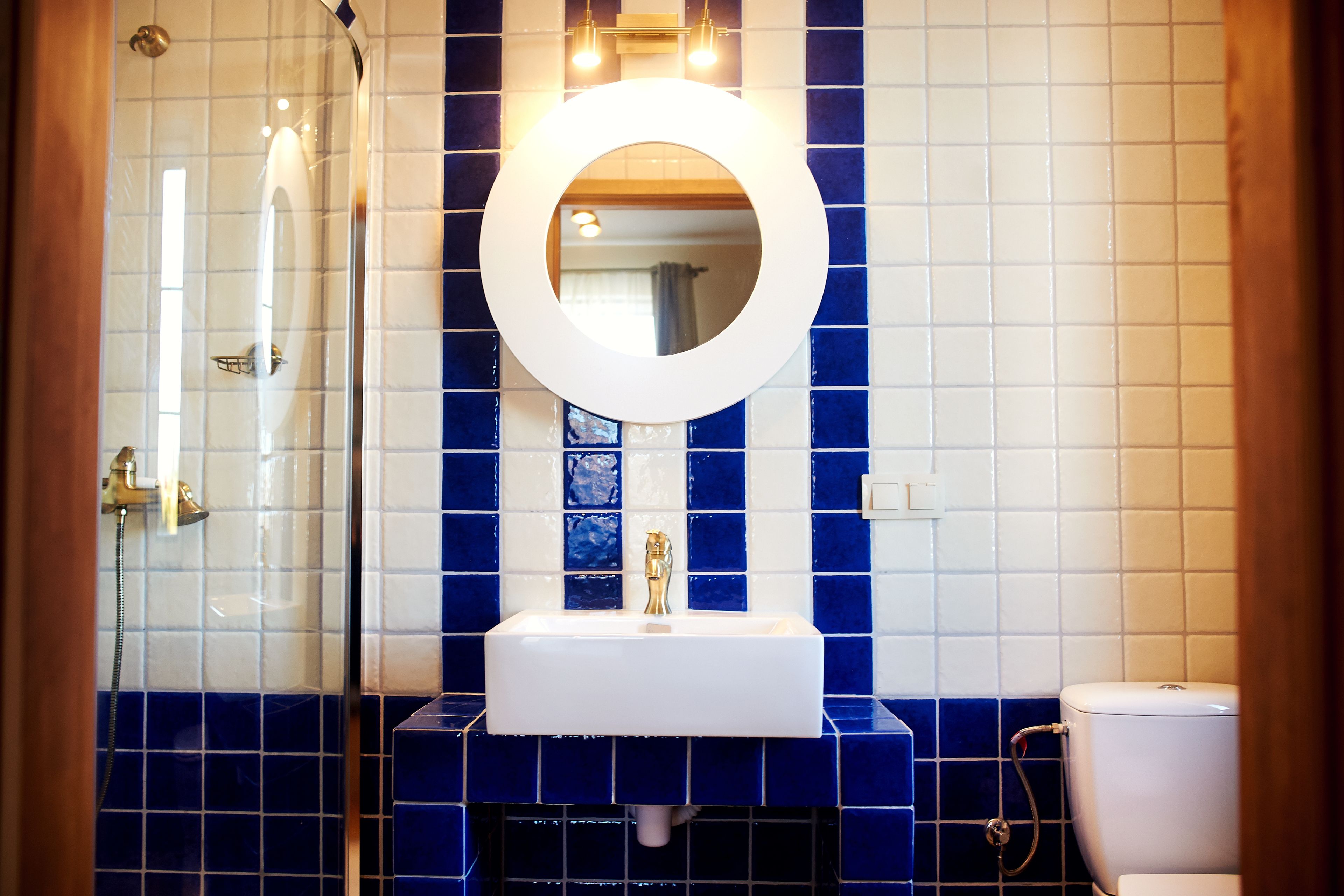 A bathroom with a white sink, a round mirror, and blue-tiled walls.