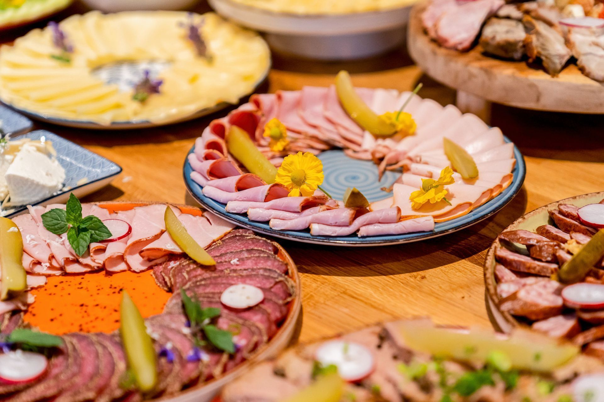 Diversos platos de comida con carnes, pepinillos y guarniciones sobre una mesa de madera.