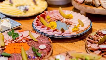 Diversos platos de comida con carnes, pepinillos y guarniciones sobre una mesa de madera.