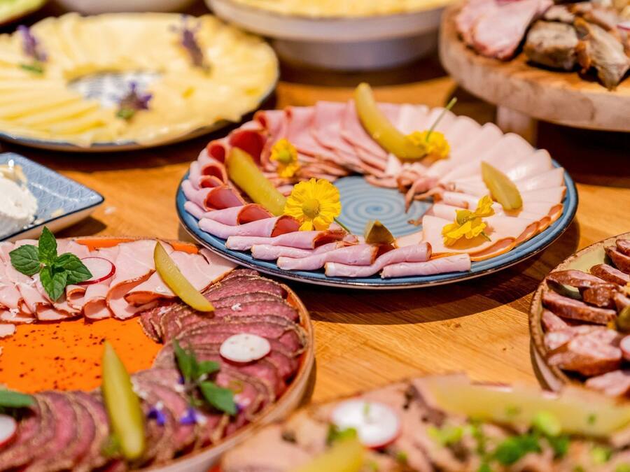 Diversos platos de comida con carnes, pepinillos y guarniciones sobre una mesa de madera.