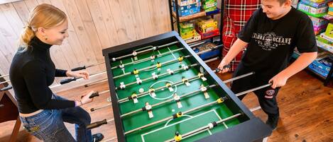 Une table de baby-foot dans une pièce au plancher en bois, avec des étagères à livres en arrière-plan.