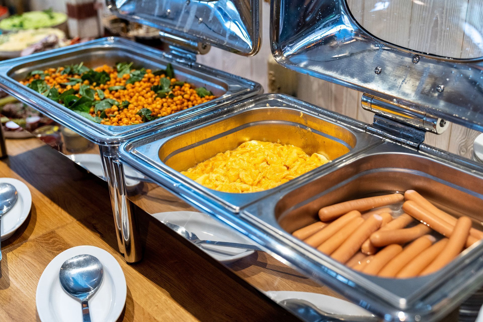 Un bufé con diversas opciones de comida, entre ellas, huevos revueltos, garbanzos y perritos calientes.