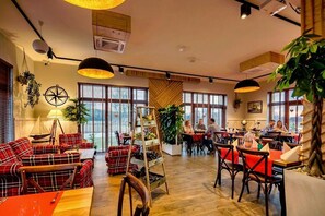 Ein gemütliches Restaurant mit Karomöbeln, großen Fenstern und Zimmerpflanzen.