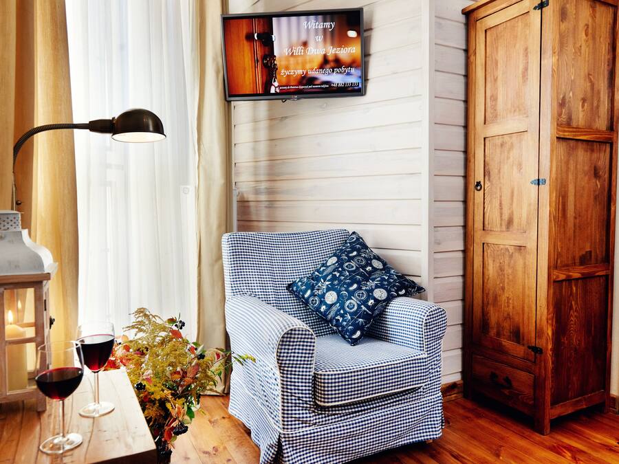 Una habitación acogedora con un sofá estampado de cuadros, un armario de madera, un televisor fijado a la pared y una mesa con una botella y vasos.