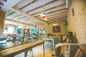 A spacious dining area with high ceilings and exposed beams, featuring multiple tables and chairs.