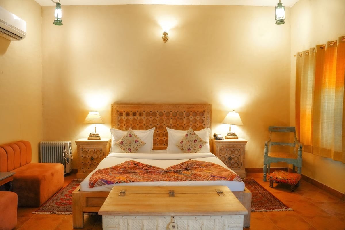 A bedroom with a large bed, two bedside lamps, a wooden headboard, a nightstand, a chair, and a small table.