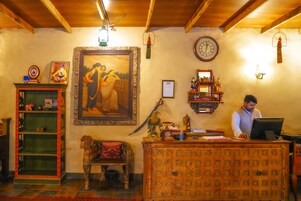 Un área de recepción con un escritorio de madera, un cuadro enmarco, un reloj y una estantería con figuritas.