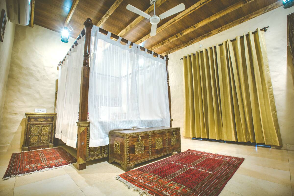 A room with a four-poster bed, a wooden chest, and a red and white patterned rug.