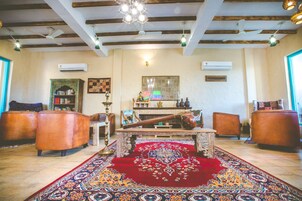 Un salón espacioso con un tapete grande y decorativo, sillones de cuero, una mesa de centro y un ventilador de techo.