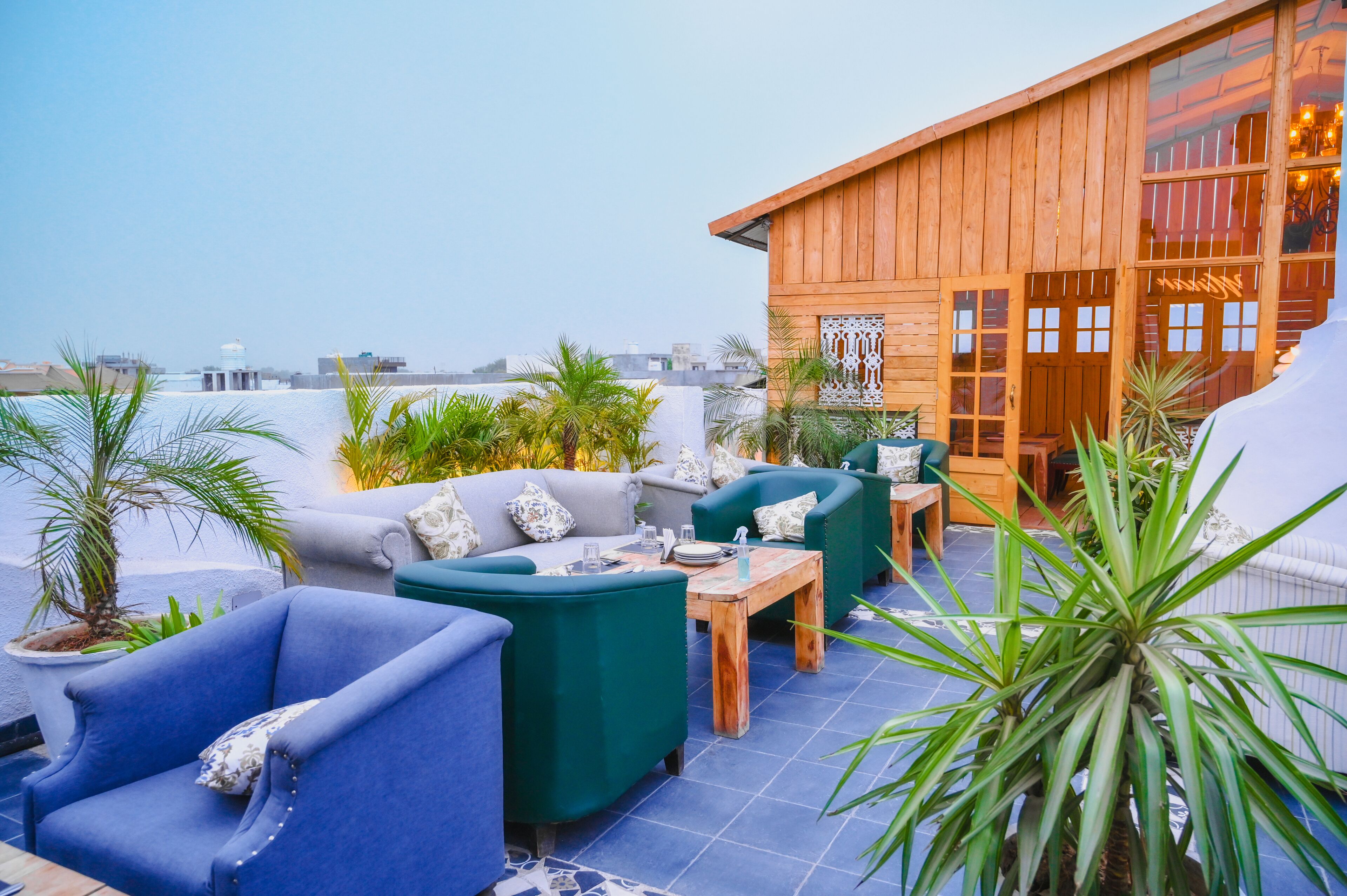 A rooftop terrace with outdoor seating, including blue and green sofas, a wooden table, and potted plants.