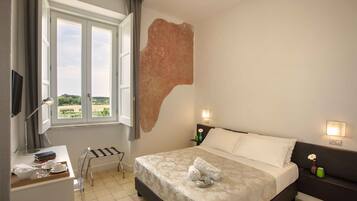 A bedroom with a bed, bedside tables, a desk, a chair, a window, and a view of greenery outside.