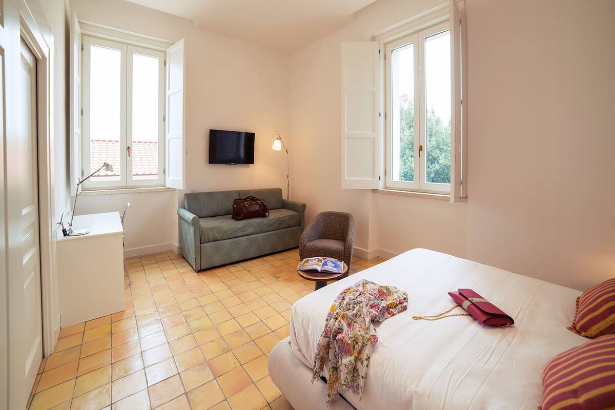 Une chambre d’hôtel avec un lit, un canapé, une chaise, une télévision et une fenêtre.
