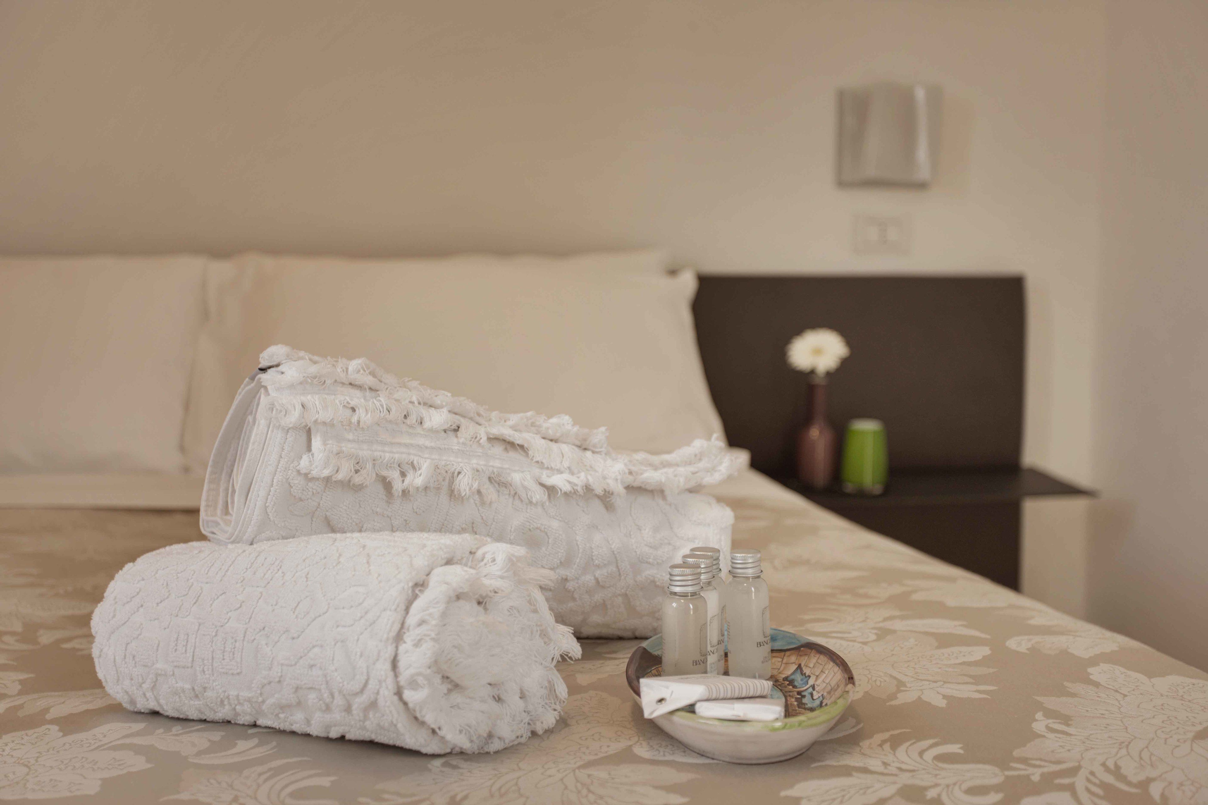 Una cama bien hecha con toallas blancas enrolladas y una bandeja con artículos de aseo.