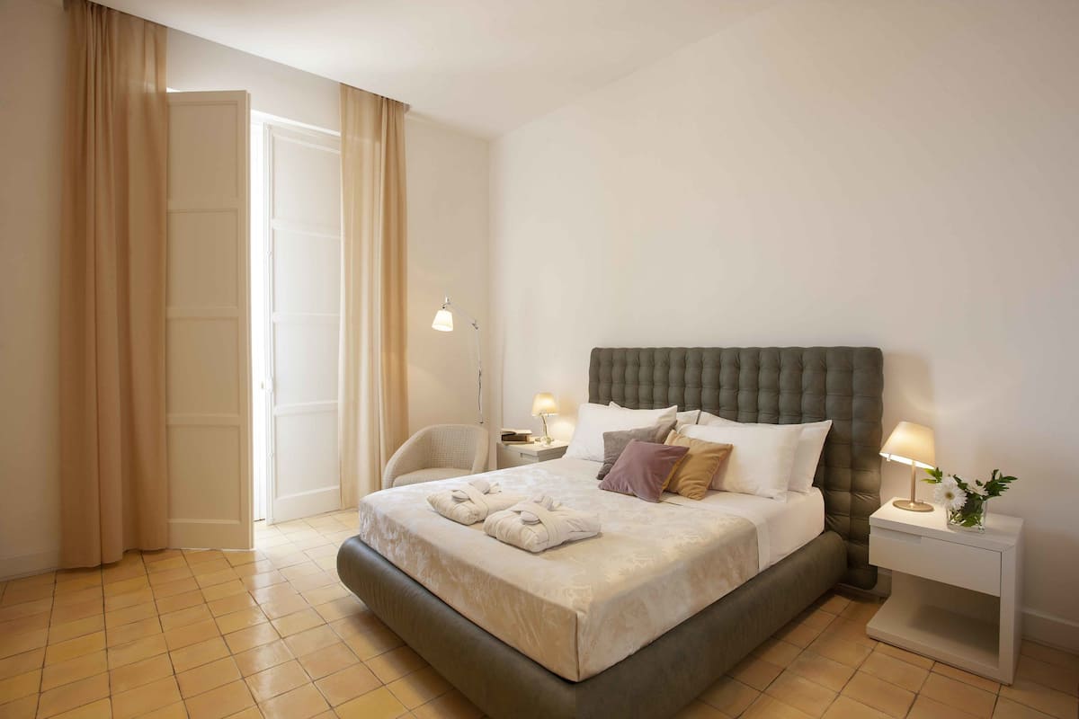 Un lit bien fait, avec une tête de lit, deux tables de chevet avec des lampes et une chaise.