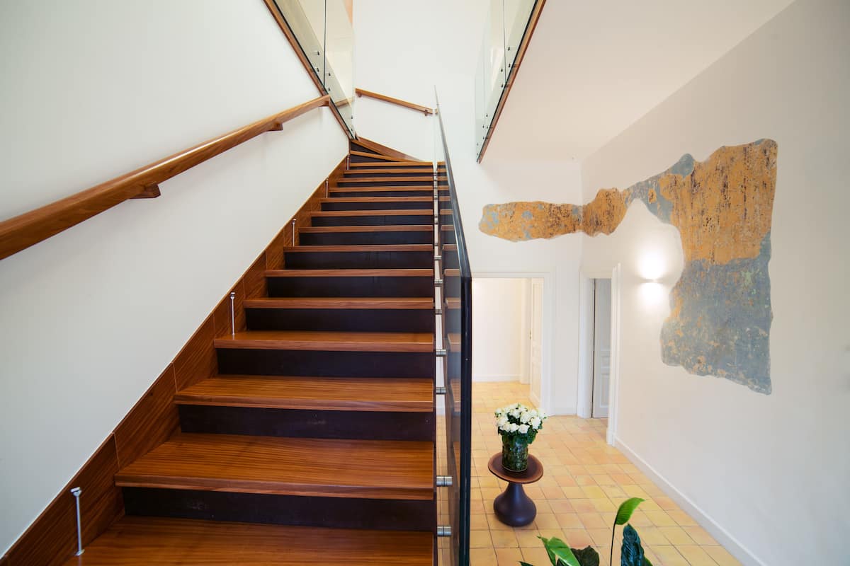 Un escalier en bois avec des rampes en verre menant à une pièce dotée d’une porte blanche et d’un élément décoratif mural.