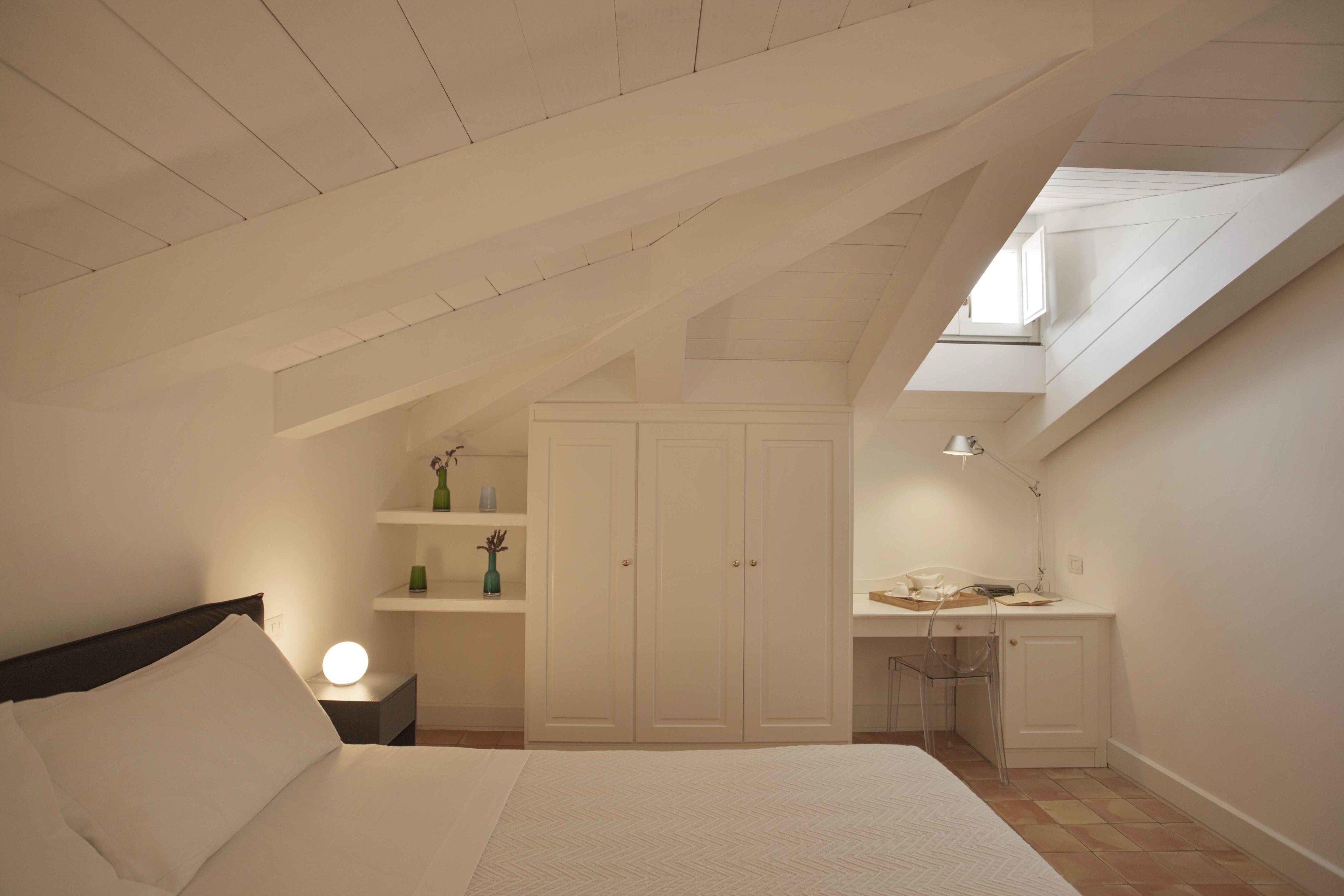 A bedroom with a sloped ceiling, a bed, a desk, and a wardrobe.