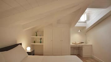 A bedroom with a sloped ceiling, a bed, a desk, and a wardrobe.