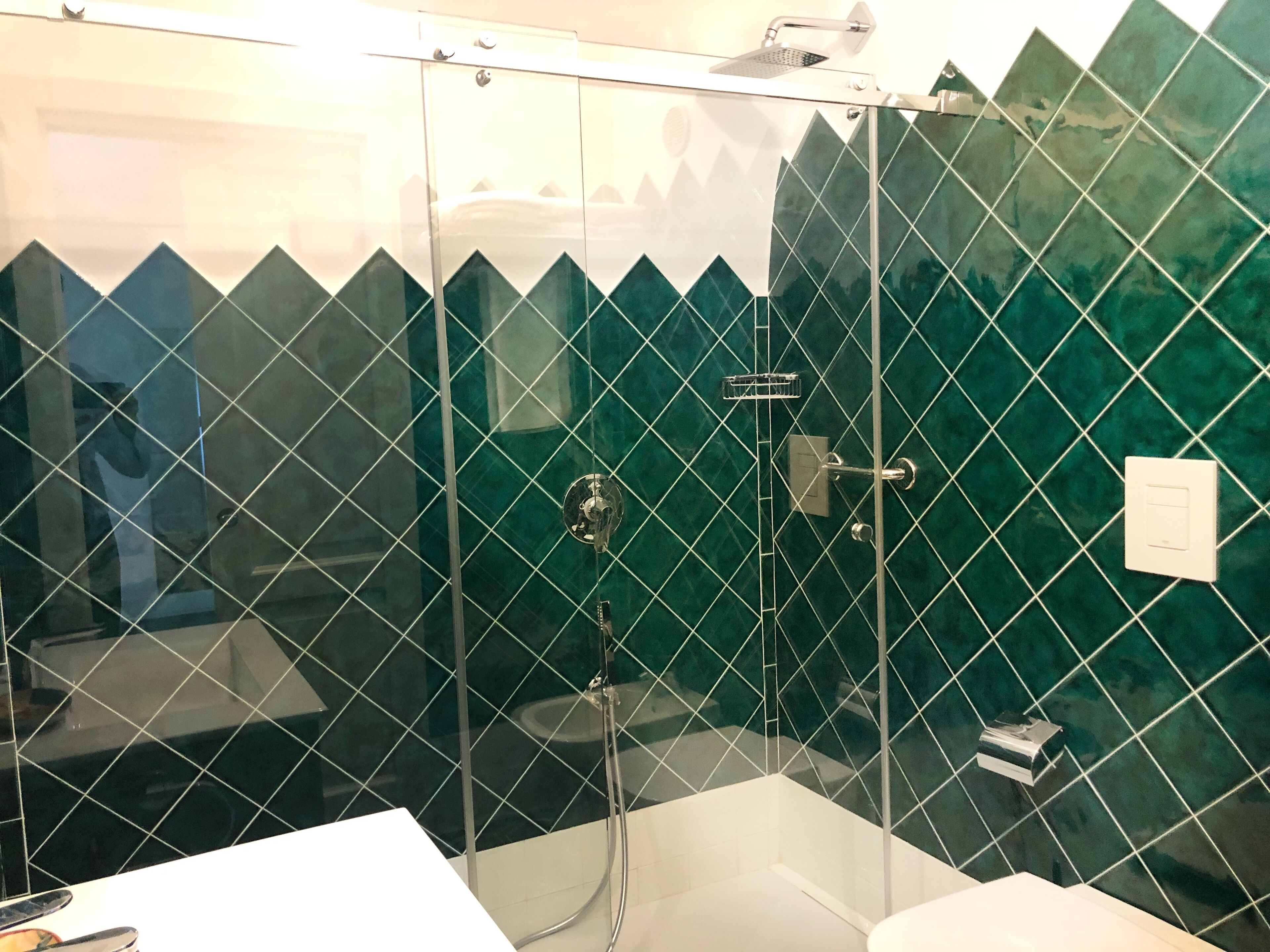 A bathroom with a glass-enclosed shower, a white sink, and green-tiled walls.