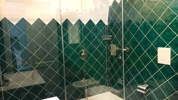 A bathroom with a glass-enclosed shower, a white sink, and green-tiled walls.