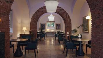Un restaurant doté d’arches en briques, de tables et de chaises rondes, avec une cheminée centrale et des œuvres d’art encadrées qui ornent les murs.