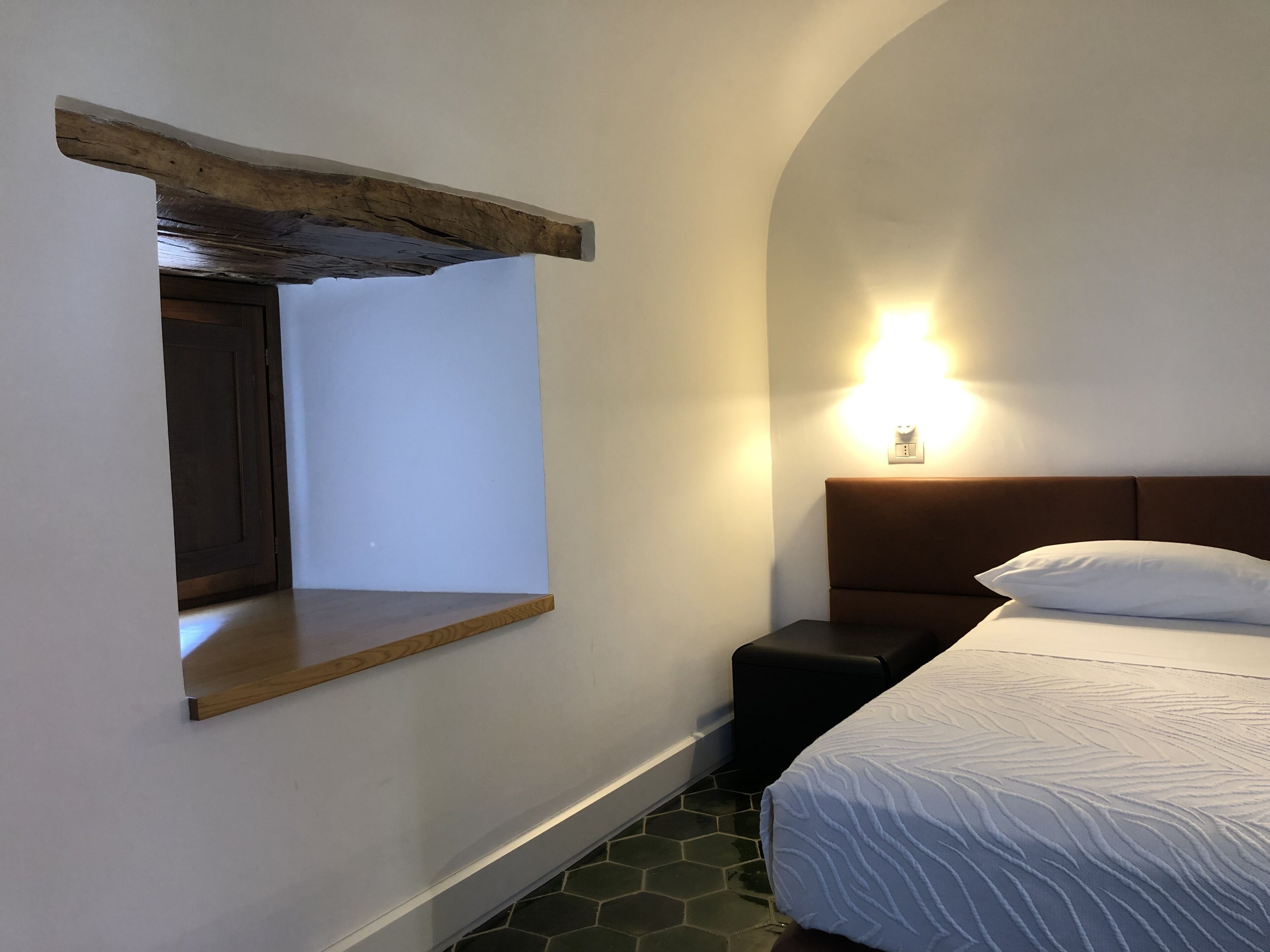 Ein Schlafzimmer mit einer Holztrennwand, einem Nachttisch, einem Bett mit weißem Kopfkissen und einer Wandleuchte.