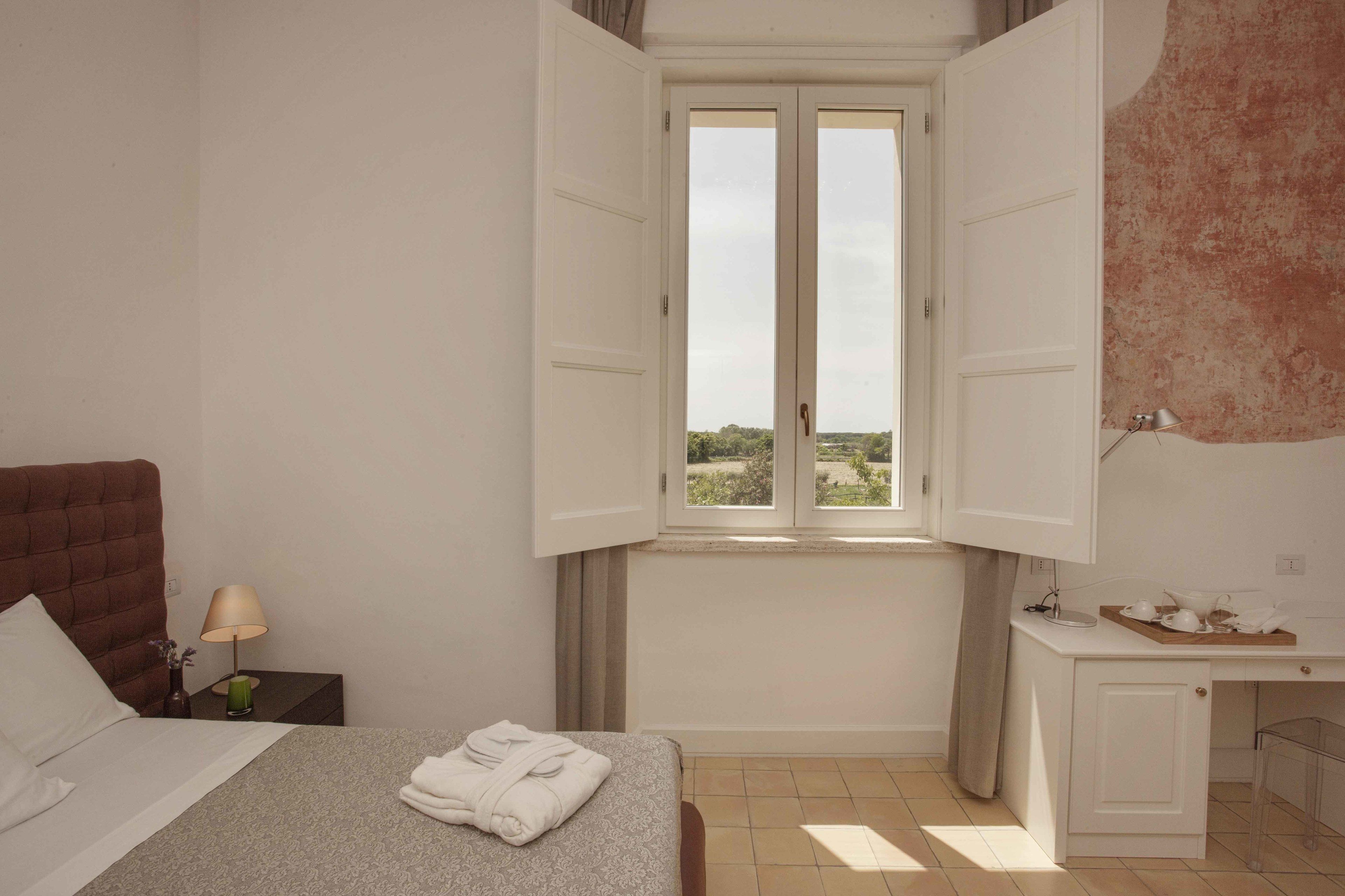Une chambre à coucher avec un lit, une table de chevet avec une lampe, une fenêtre avec des rideaux et un bureau avec un plateau.