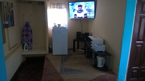 A small, narrow room with a refrigerator, a microwave, a toaster, and a television mounted on the wall. - Mambilima Furnished Guest Wing (Lusaka)