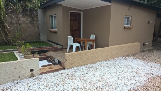 A small house with a patio, a wooden table, two white chairs, and a door. - Mambilima Furnished Guest Wing (Lusaka)