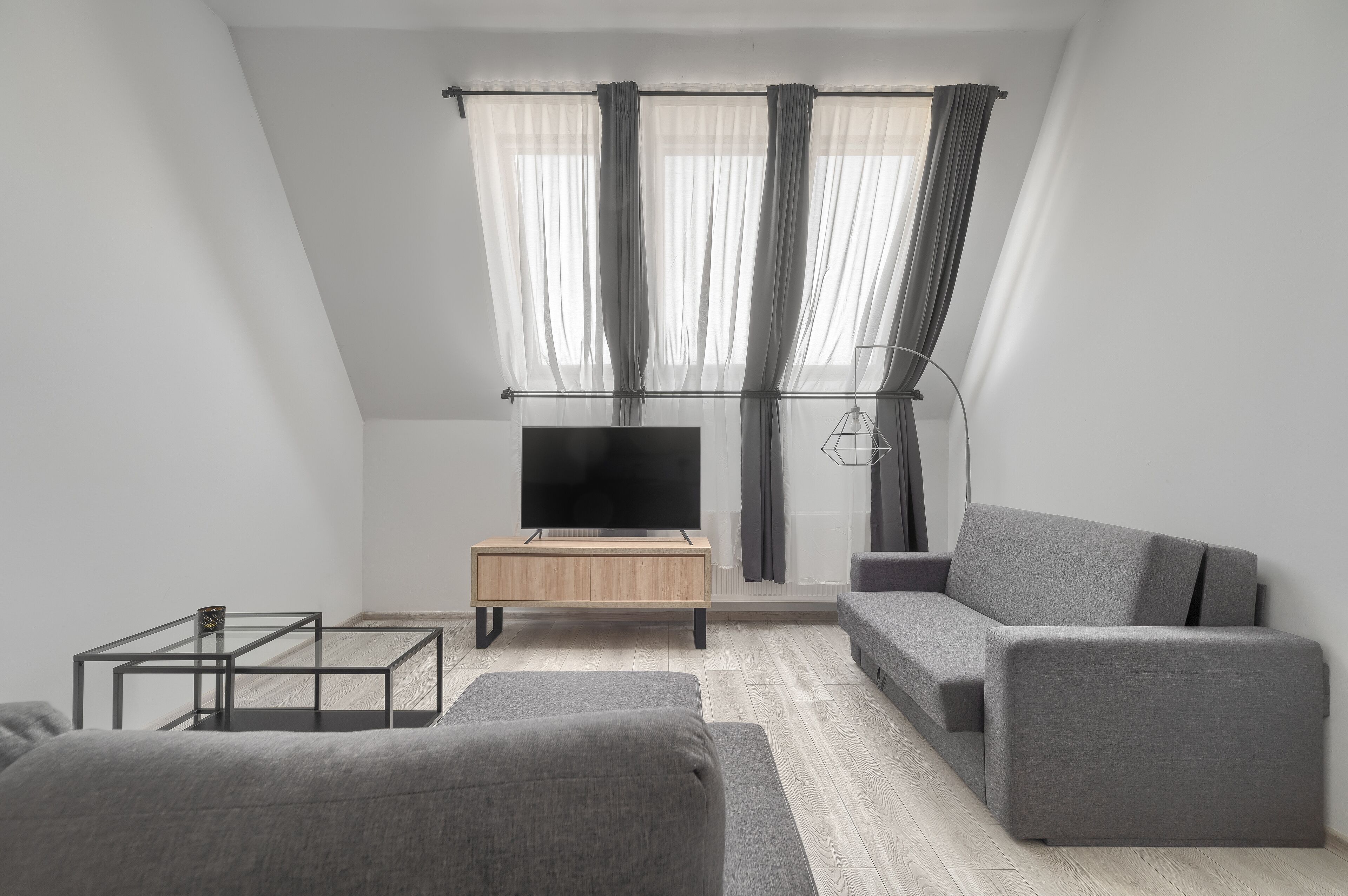 Un salon moderne avec un téléviseur à écran plat, un canapé gris et une table basse en bois.