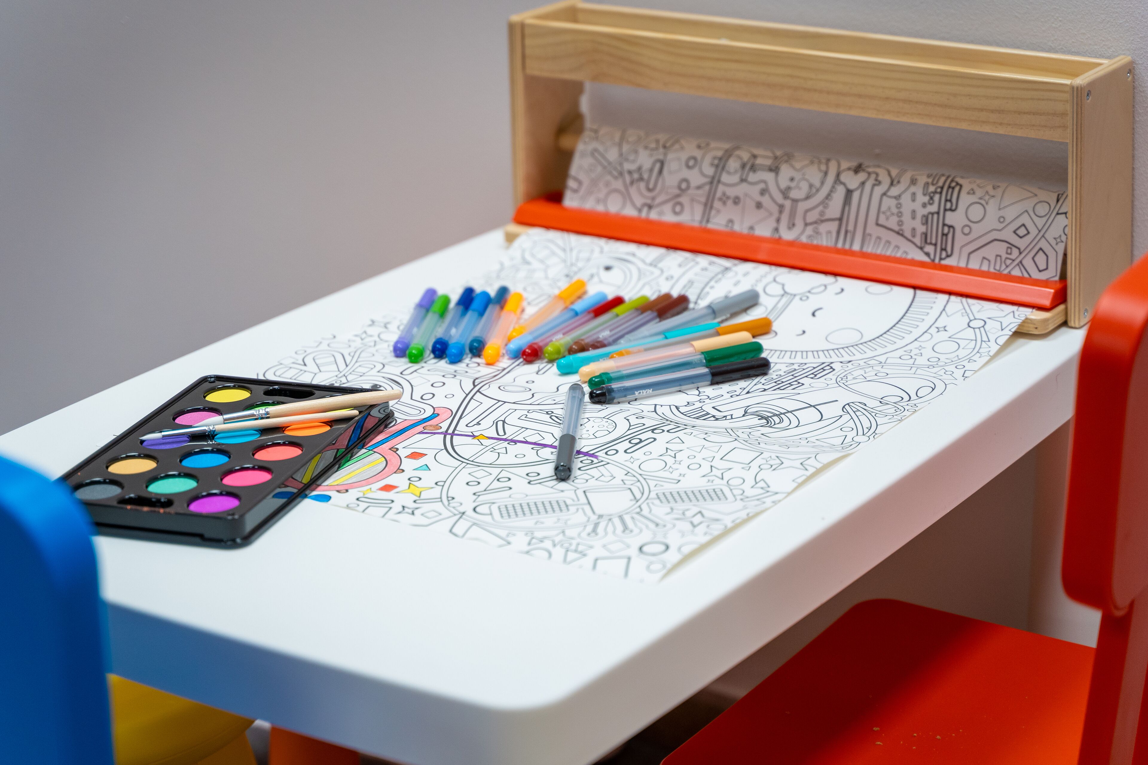 Una mesa con un libro para colorear, marcadores y acuarelas.