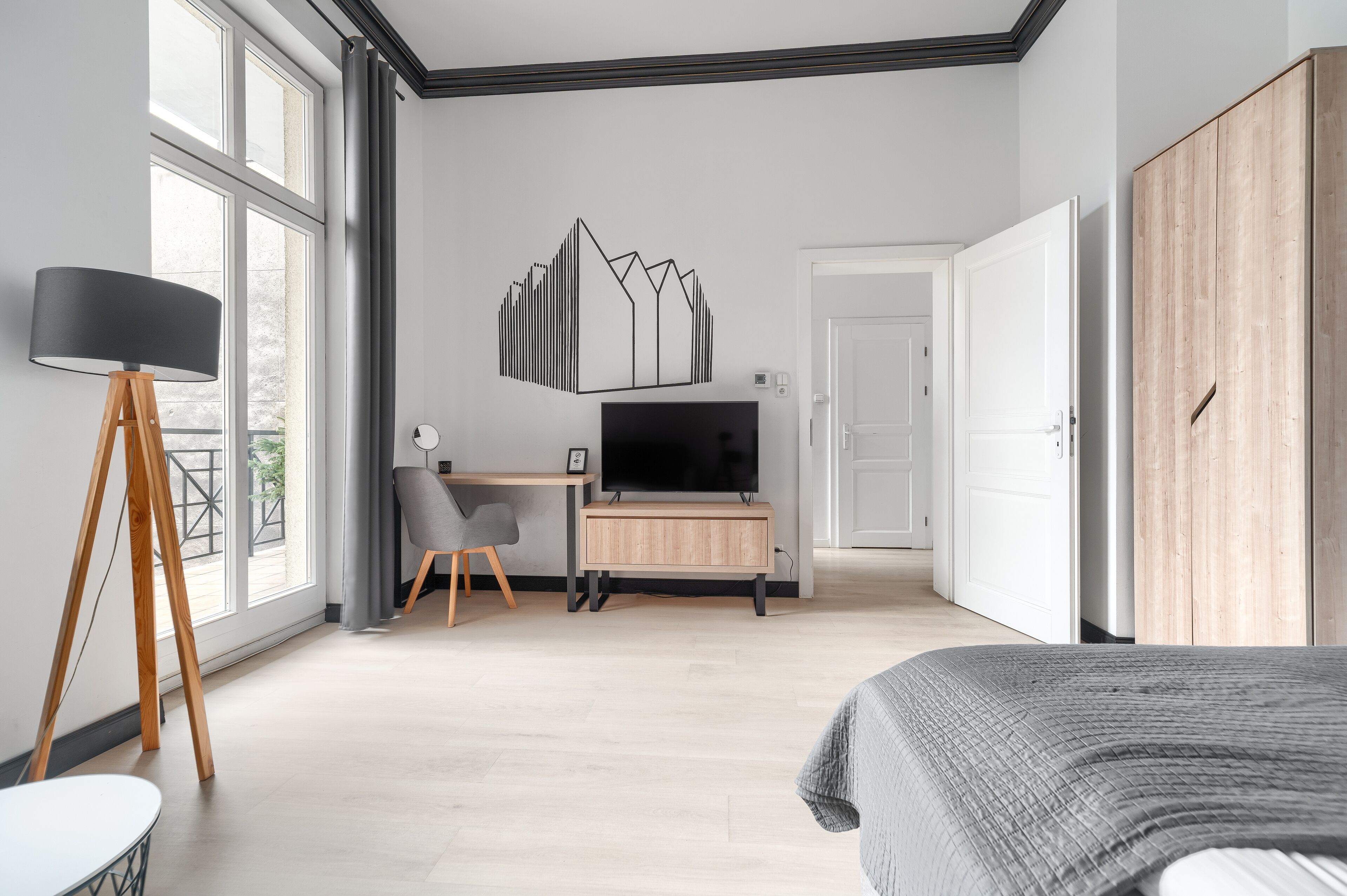 Ein modernes Schlafzimmer mit einem Bett, einem Schreibtisch mit Fernseher, einem Kleiderschrank und großen Fenstern.