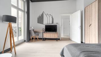Ein modernes Schlafzimmer mit einem Bett, einem Schreibtisch mit Fernseher, einem Kleiderschrank und großen Fenstern.