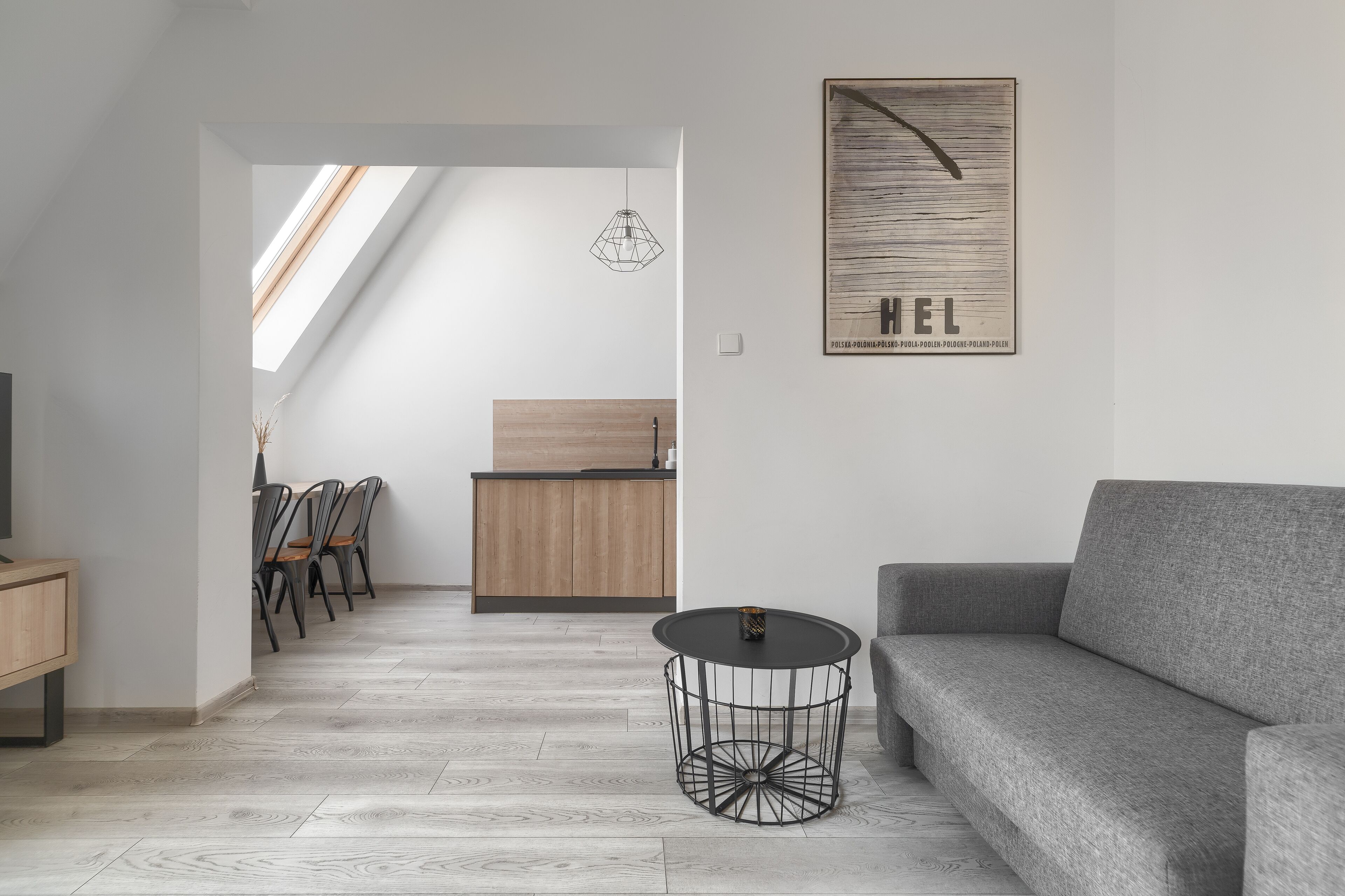 Un soggiorno moderno con un divano grigio, un tavolo nero rotondo e un'area pranzo in legno con sedie.