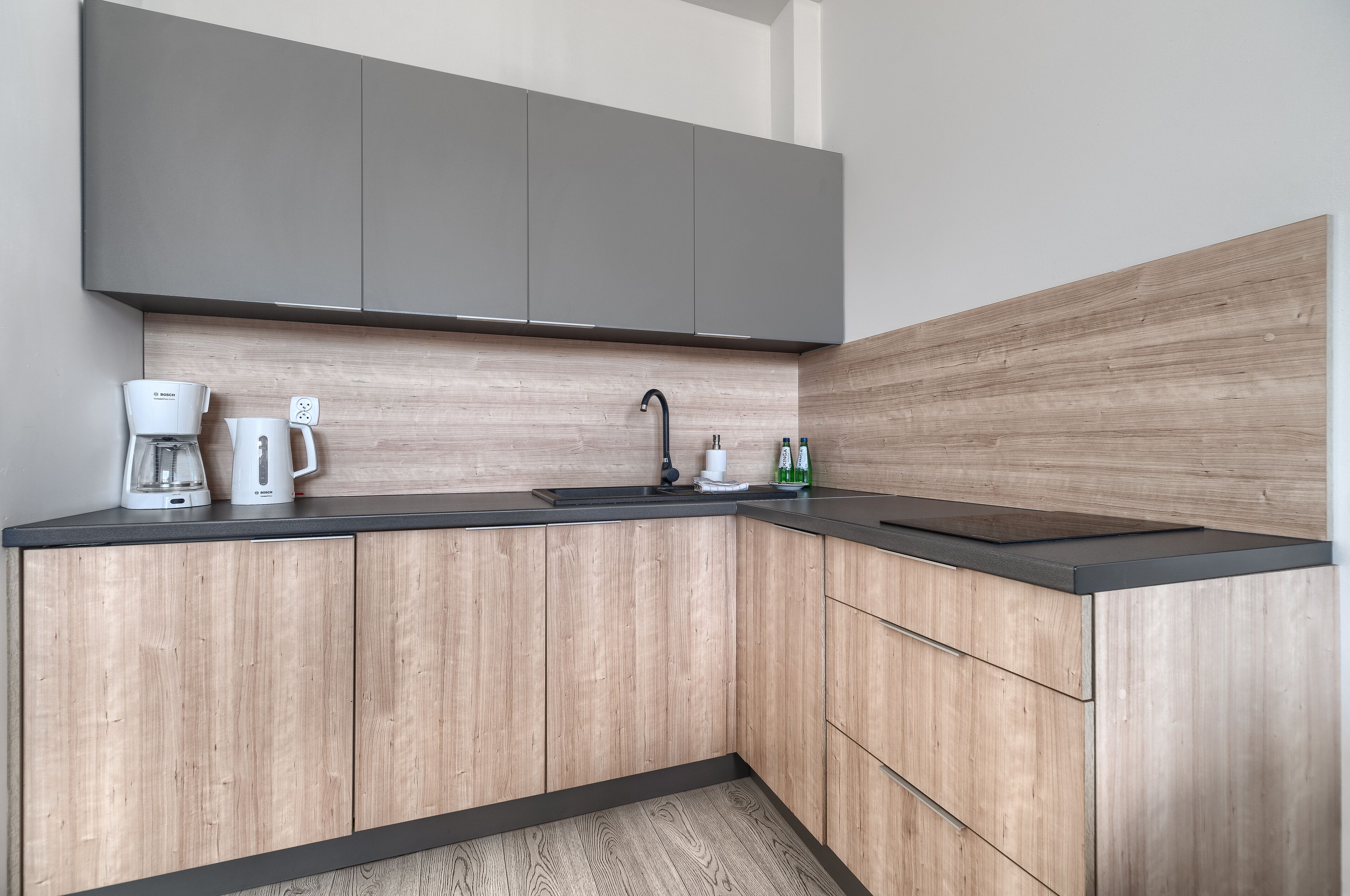 Una cocina moderna con armarios de madera, una encimera negra, una cafetera y un lavabo.