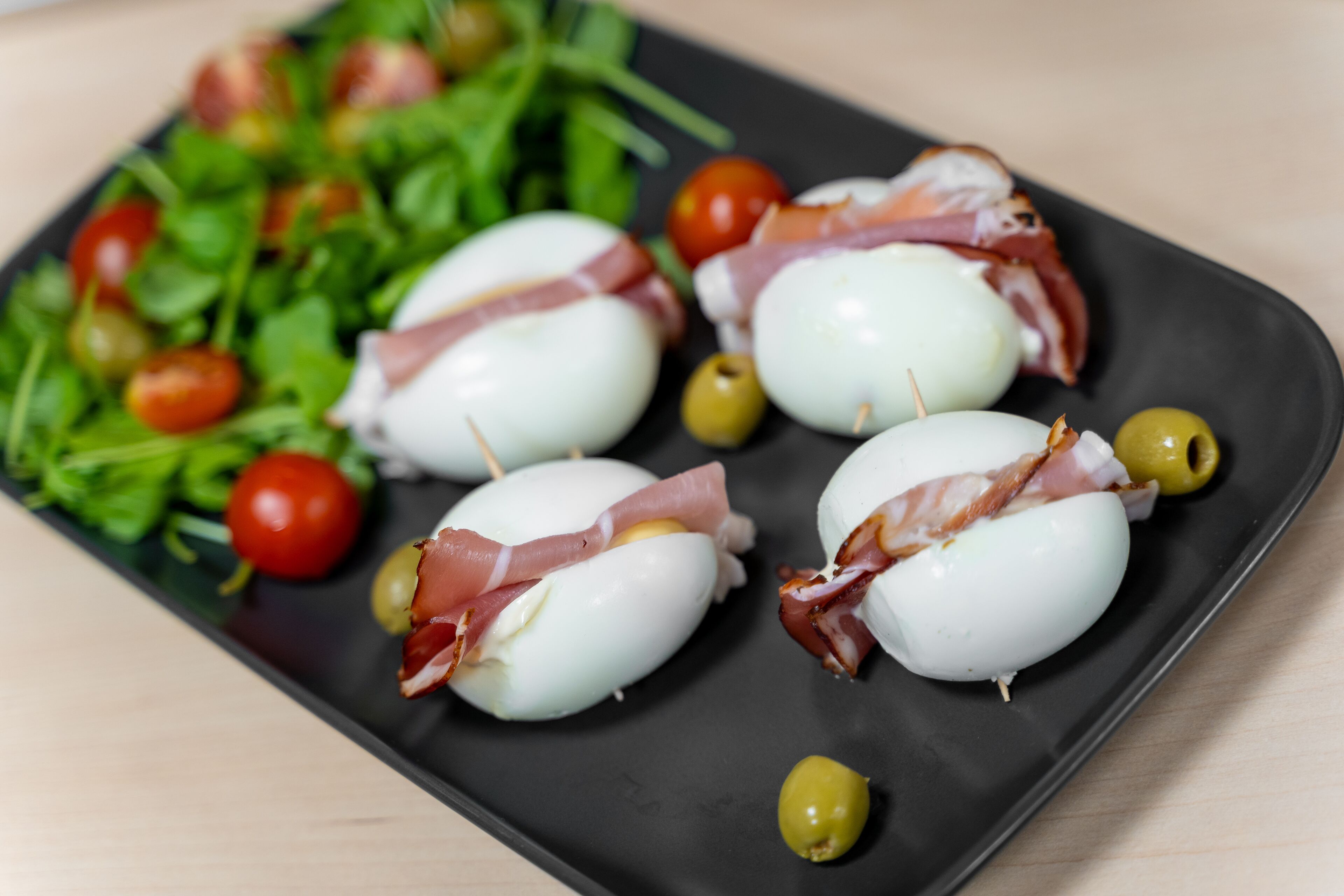 Un piatto nero con bocconcini di mozzarella, prosciutto e olive.