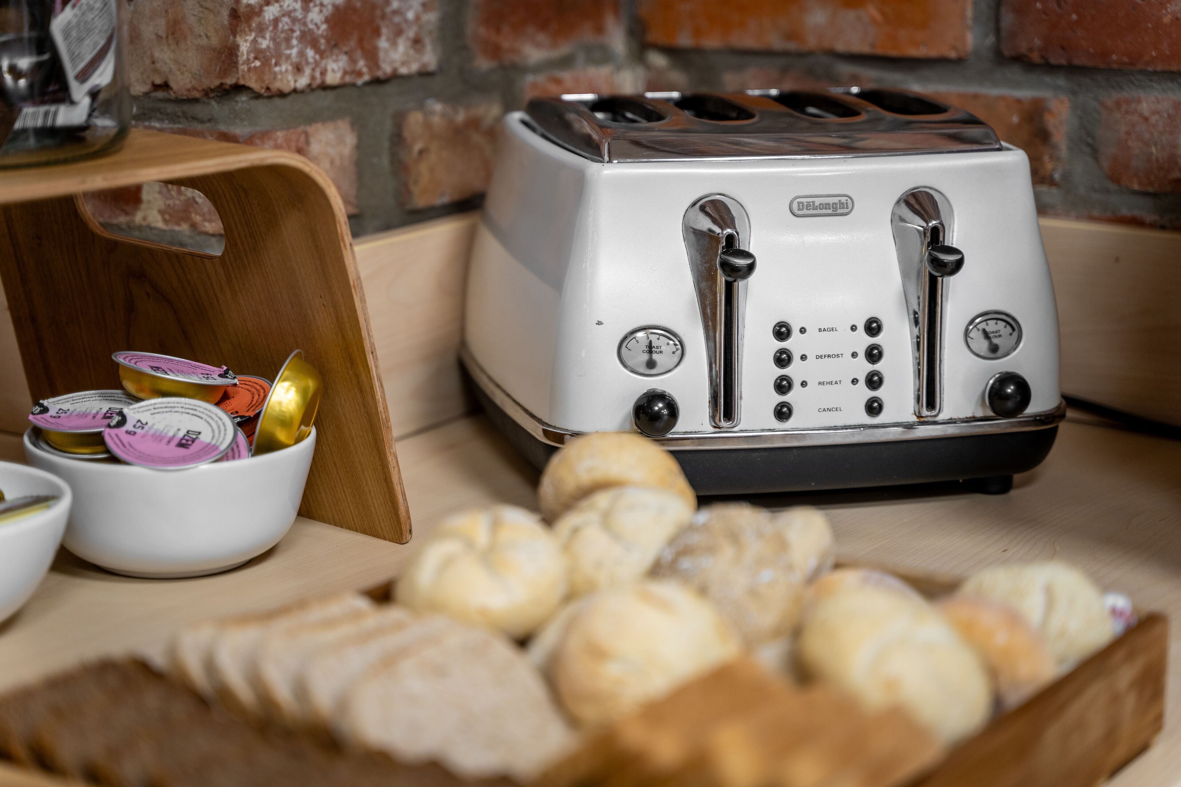 A vintage Oster toaster with multiple slots, a wooden cutting board with condiments, and a basket of bread.