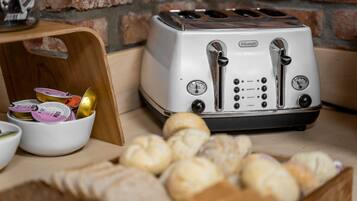 A vintage Oster toaster with multiple slots, a wooden cutting board with condiments, and a basket of bread.