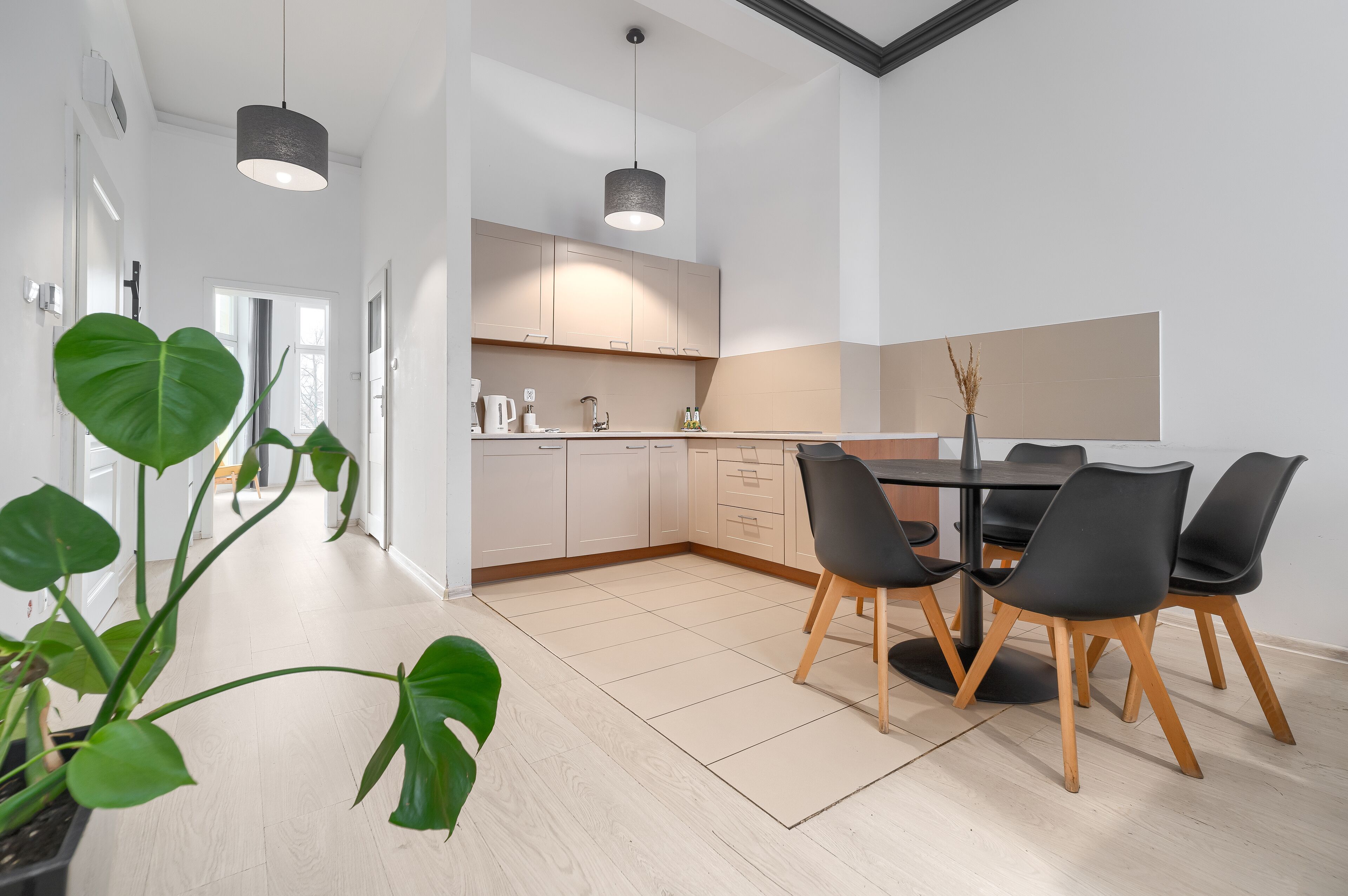 Una cocina moderna con armarios blancos, una mesa de comedor con sillas negras e iluminación colgante.