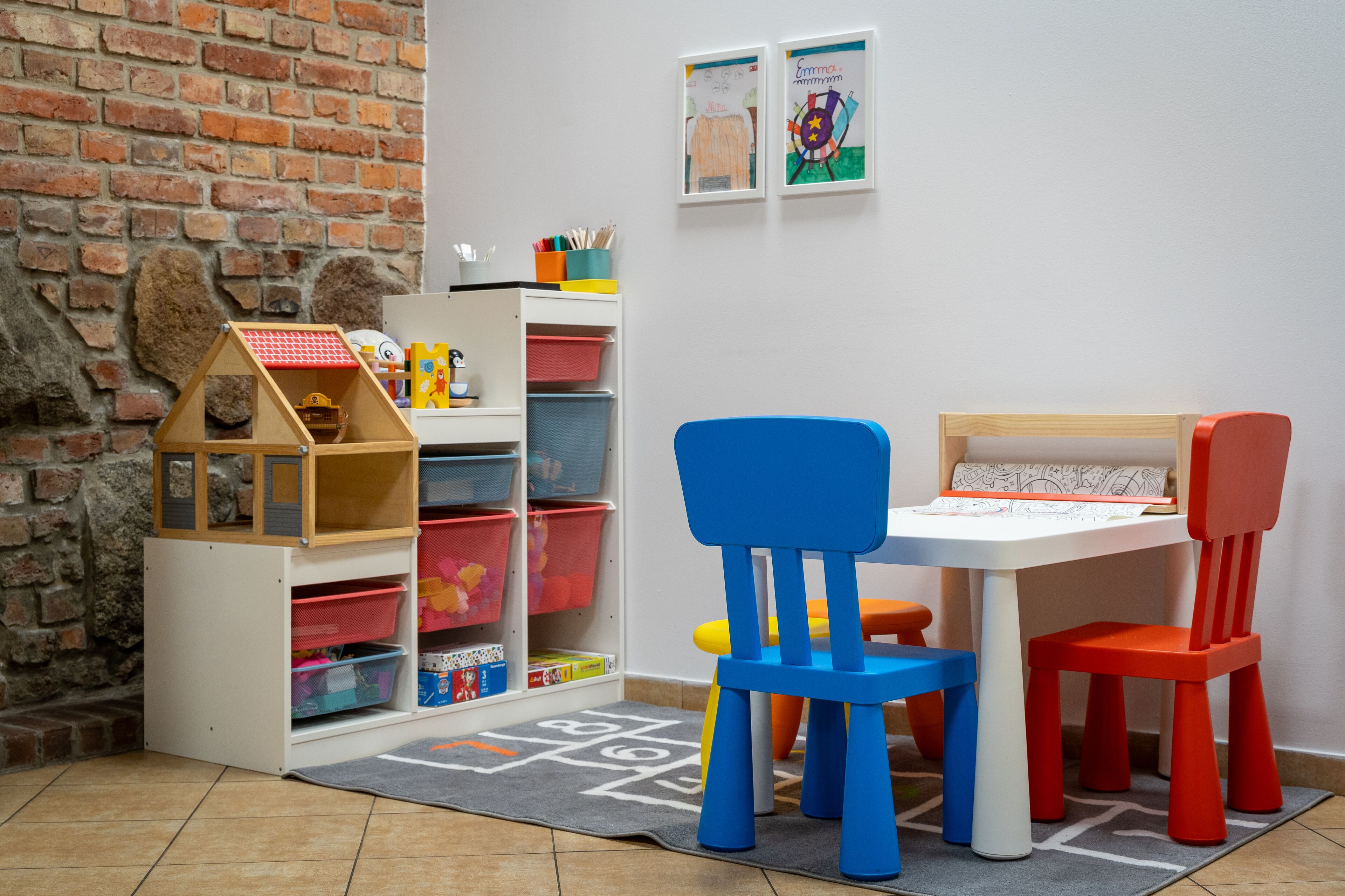 Un'area giochi per bambini con un muro in mattoni, contenitori portaoggetti e sedie colorate.