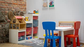 Un'area giochi per bambini con un muro in mattoni, contenitori portaoggetti e sedie colorate.