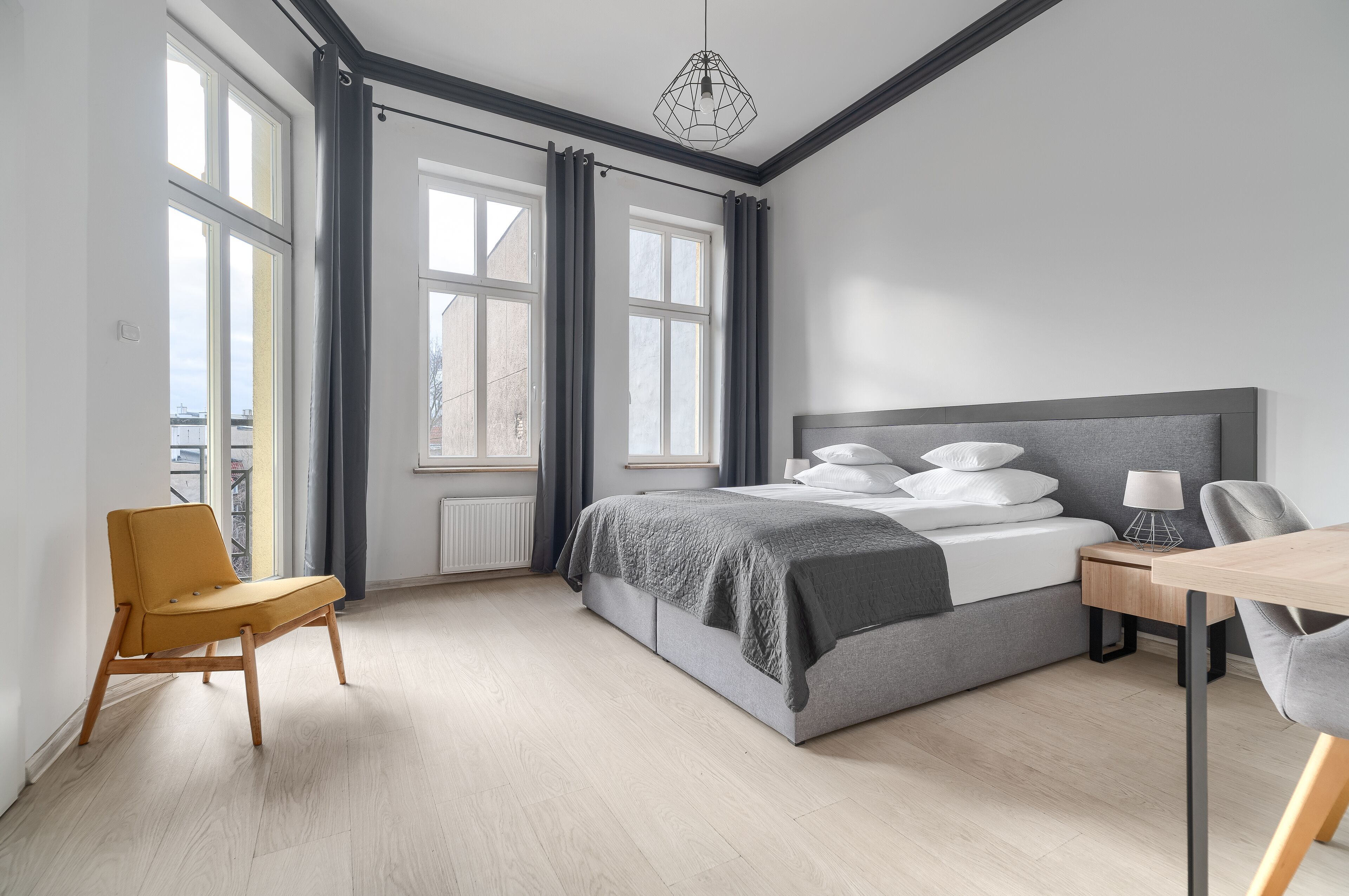 Un dormitorio moderno con cama, una silla, una mesa y ventanas amplias.