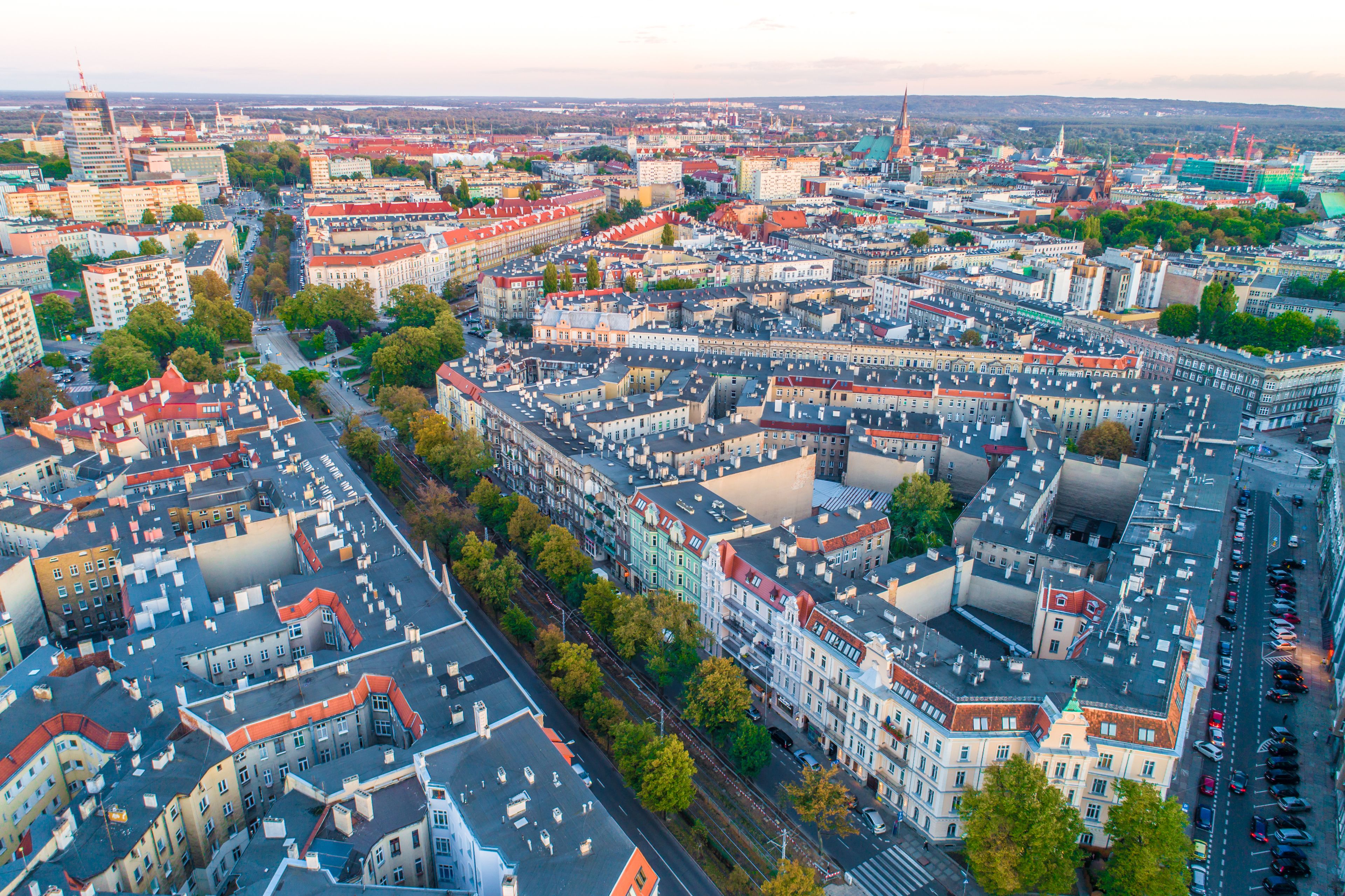 An aerial view of a densely packed urban area with a mix of historic and modern buildings, narrow streets, and a prominent church spire.