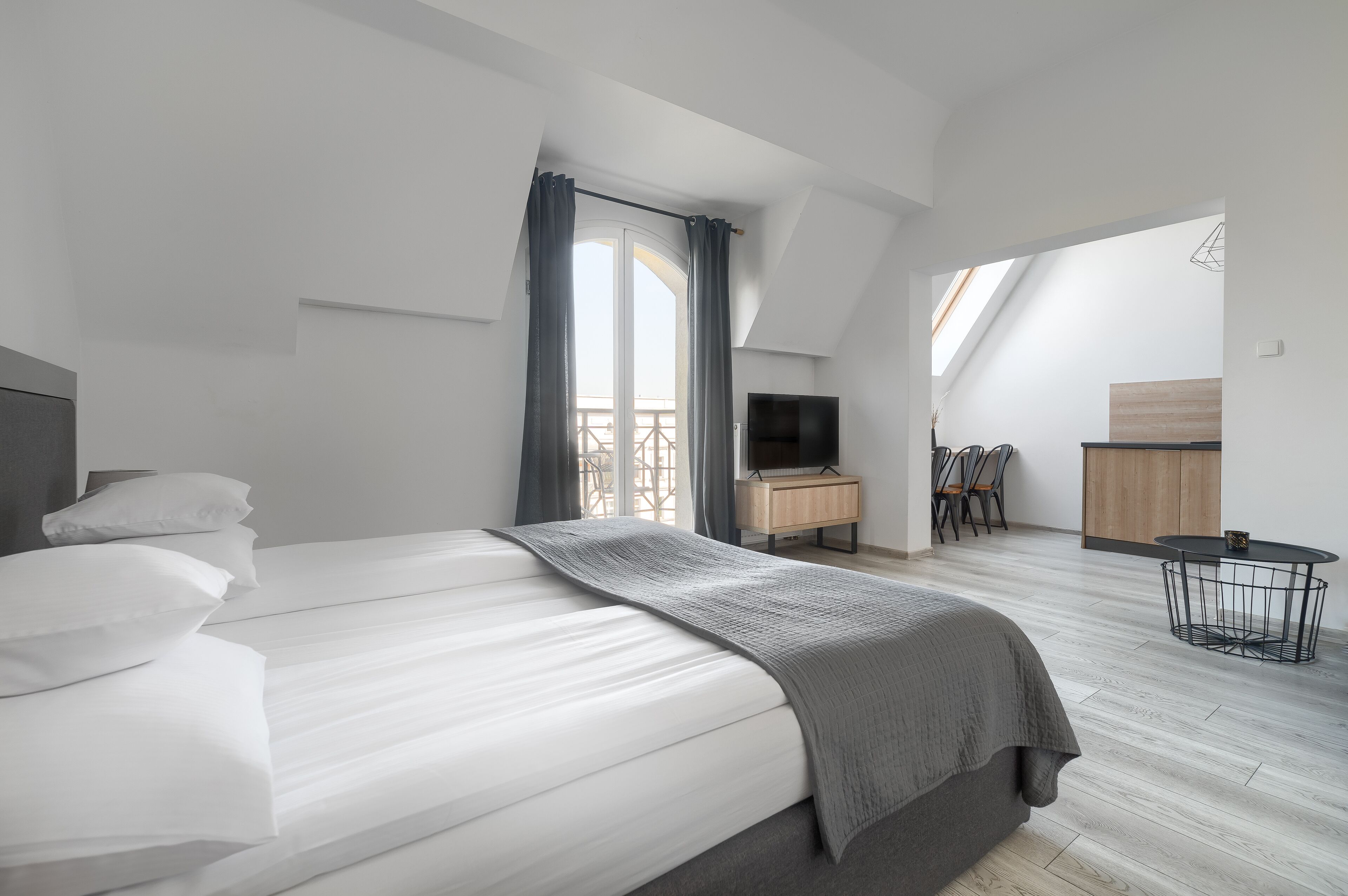 A modern hotel room with a large bed, a desk, a TV, and a balcony with a view.
